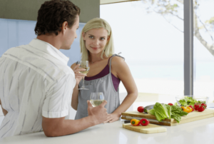 a man and woman flirting in the kitchen while drinking a glass of wine